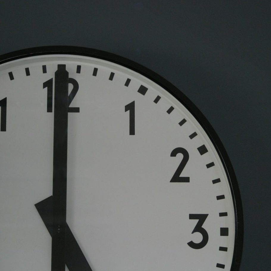 Uhr mit schwarzen Zeigern, kurz vor zwölf, auf dunklem Hintergrund.